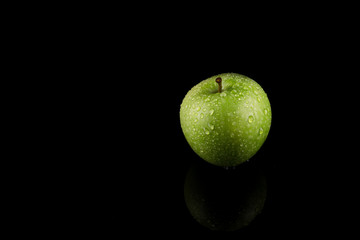 Green Apples with water drops on reflective table, isolated on dark background.copy space.