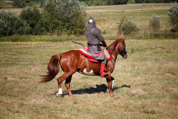 Reconstruction. Medieval armored knight on white horse from fantasy. Equestrian soldier in historical costume. Reenactor is in the field