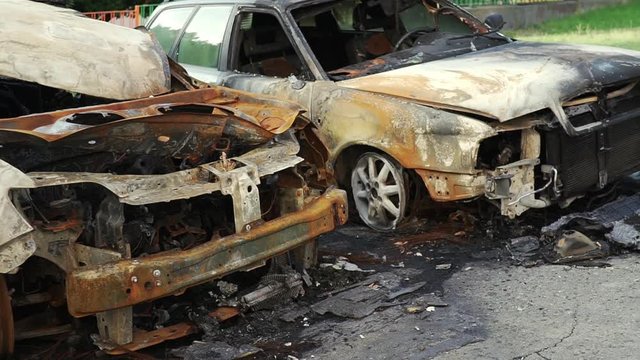 A slide slow motion  of two passenger cars burned down, which suffered from a violent fire in a city parking lot on a street in a big city. Damaged vehicle surface. An incident in the parking of cars