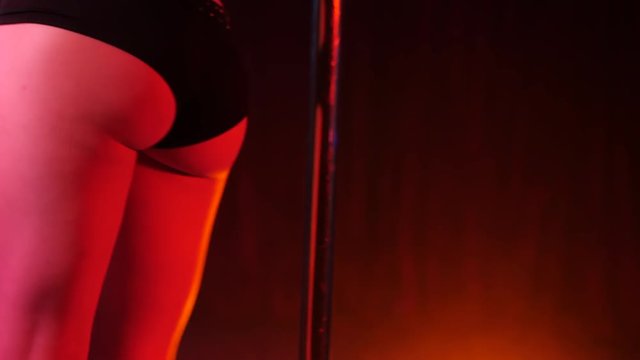 Sexy woman in black costume. Striptease dancer moving buttocks on dark neon smoke stage in night club with pylone. Strong and graceful lady seduces visitors