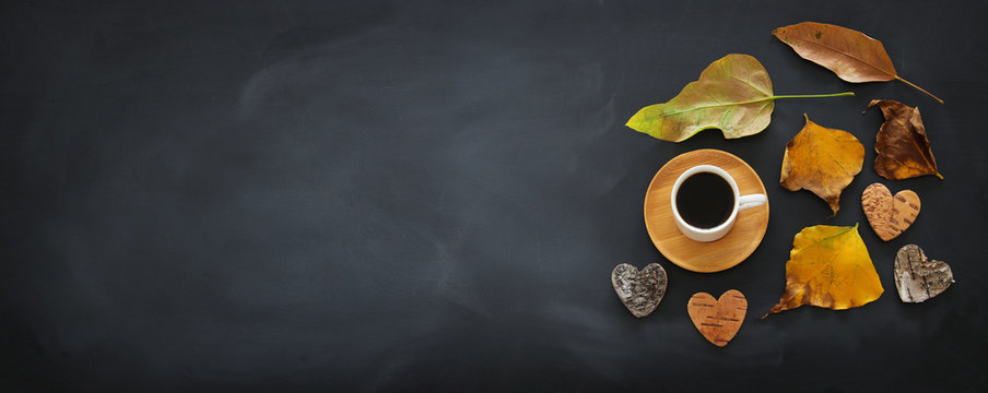top view banner of coffee cup over blackboard background and dry autumn leaves.