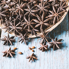 Whole star anise in a basket and spoon with seeds on blue rustic wooden background, indian spice.