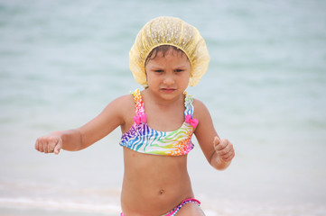 a little girl in a shower cap runs out of the sea