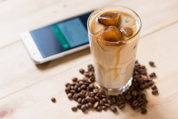 Espresso coffee frozen into ice cube mixed with milk on wooden background, smartphone placed on the table for business concept