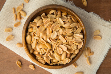Roasted peanuts in wooden bowl putting on linen and wooden background. © Touchr