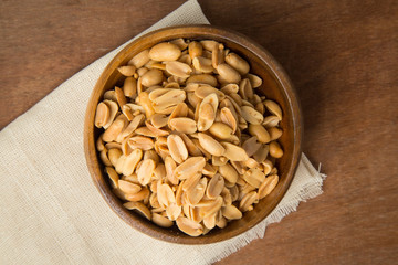 Roasted peanuts in wooden bowl putting on linen and wooden background.