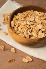 Roasted peanuts in wooden bowl putting on linen and wooden background.