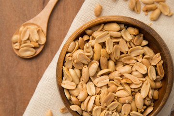 Roasted peanuts in wooden bowl and spoon putting on linen and wooden background.