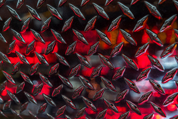 Close up of stainless steel sheet with diamond plate pattern and reflecting red lights / Metallic background