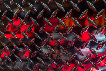 Close up of stainless steel sheet with diamond plate pattern and reflecting red lights / Metallic...