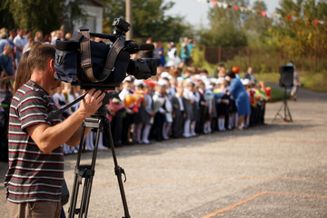 Professional cameraman covering on event. Professional cameraman covering on event. Blurred abstract background image with students and teachers at the school meeting on the day of knowledge