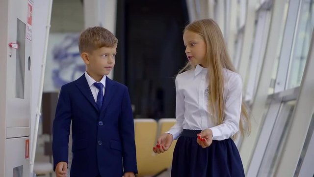 Handsome young boy in a suit and cute girl in a skirt talking while walking indoor.