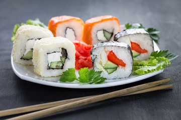 Sushi on a square white plate with parsley and chopsticks. Close up. Gray background