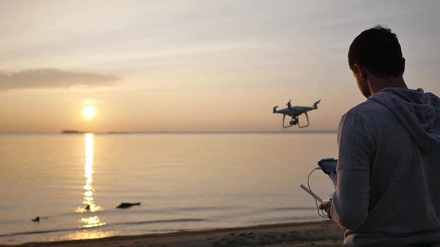 A man controls a drone at sunset