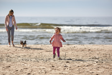 young blode woman mother is playing with a girl daughter and yorkshire dog puppy in summer spring at the beach