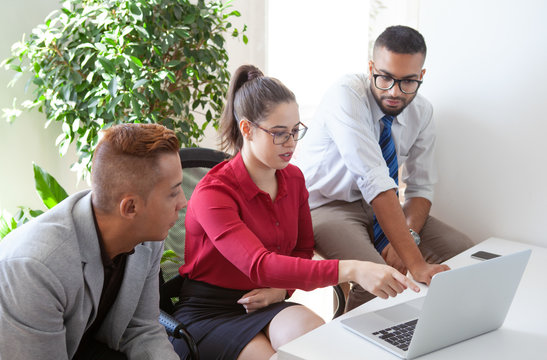 Serious accountant giving advice to two business leaders. Woman in formal clothes and glasses sitting at workplace, pointing at laptop screen and explaining data to two colleagues. Expertise concept