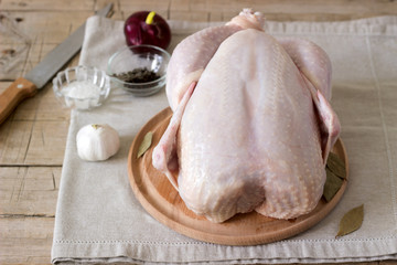 Raw chicken on a wooden board with spices and vegetables.