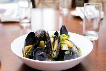 Mussels in shells in a white bowl with a green sauce on a dining table.