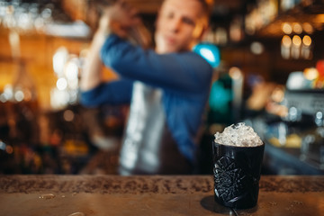 Black glass full of ice stands on bar counter