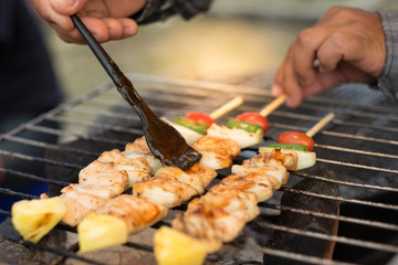  hand hold brush take sauce on barbecue and roast pork with  vegetable , slice papaya , green pepper, onion, on grille charcoal stove . thai street food