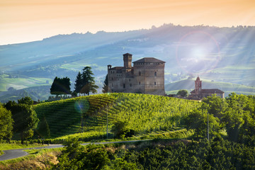 View on the castle of Grinzane cavour at Sunset, the sky is yellow and orange and some sunrays illuminate the Manor in backlight