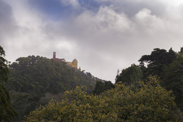 Fototapeta na wymiar Pena Palace on green hill in forest in Sintra, Portugal with clouds