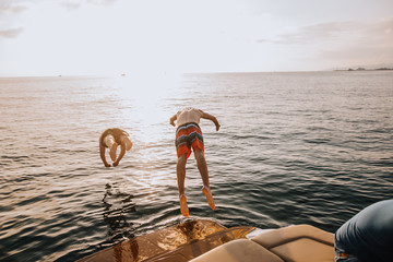 Two happy caucasian male friends traveling on a yacht at open sea, jumping in the water from the...