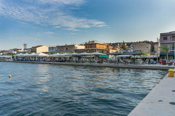 Fototapeta premium Panoramic sunset view of Argostoli city in Kefalonia Greece. View of the port and the traditional houses. People enjoying their coffee or food along the embankment