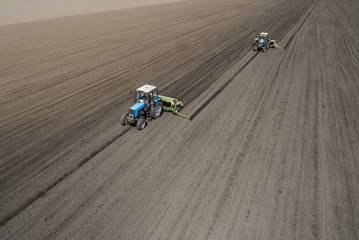 Aerial view of two blue tractors plows the earth in field on a summer day against a black earth background. Agriculture. Two tractors travel one after another along the black field