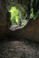 Hombre de pie dentro de una impresionante cueva de paredes de intenso color verdes mirando hacia el bosque exterior. Cueva del Ibón, Valle de Roncal, España. 