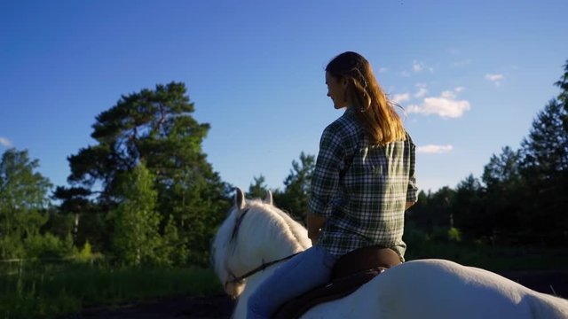 Young woman riding horse on country road during summer sunset