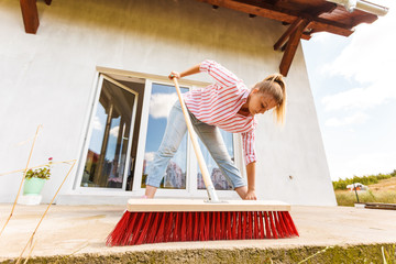 Woman cleaning patio using brush broom
