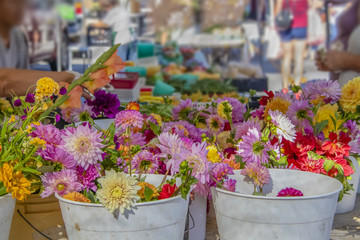 Bright beautiful flowers in buckets of water in focus in foreground with blurred - bokeh busy outdoor market stretching out behind