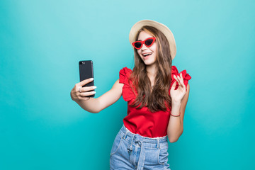 Portrait of an excited beautiful woman wearing dress looking at mobile phone and celebrating over blue background