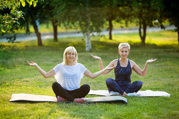 two adult women aged yoga outdoors in summer in the park