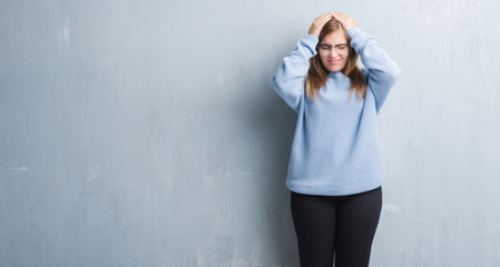 Young adult woman over grey grunge wall wearing glasses suffering from headache desperate and stressed because pain and migraine. Hands on head.