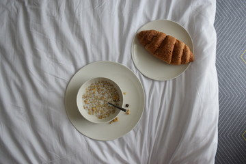 Breakfast on the white bed. Muesli and croissant