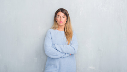 Young adult woman over grey grunge wall wearing winter outfit with serious expression on face. Simple and natural looking at the camera.