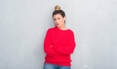 Young adult woman over grey grunge wall wearing winter outfit skeptic and nervous, disapproving expression on face with crossed arms. Negative person.