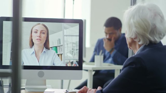 Medium shot of senior woman seen from her back having video chat with young colleague in office