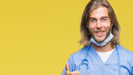 Young handsome doctor man with long hair over isolated background doing happy thumbs up gesture with hand. Approving expression looking at the camera with showing success.
