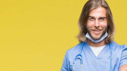 Young handsome doctor man with long hair over isolated background smiling friendly offering handshake as greeting and welcoming. Successful business.