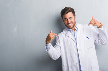 Handsome young professional man over grey grunge wall wearing white coat looking confident with smile on face, pointing oneself with fingers proud and happy.