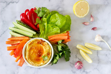 Hummus, different vegetables and lettuce leaves with lemon and garlic on a light background. Vegan food.