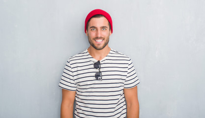 Fototapeta premium Handsome young hipster man over grey grunge wall wearing navy t-shirt and wool cap with a happy and cool smile on face. Lucky person.