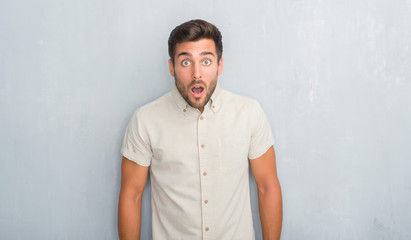 Handsome young man over grey grunge wall wearing summer shirt afraid and shocked with surprise expression, fear and excited face.