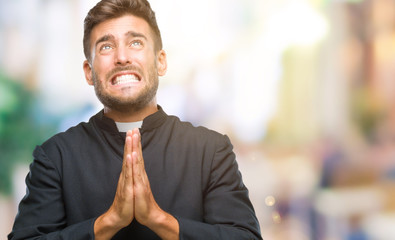 Young catholic christian priest man over isolated background begging and praying with hands...