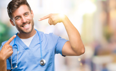 Young handsome doctor surgeon man over isolated background smiling confident showing and pointing with fingers teeth and mouth. Health concept.