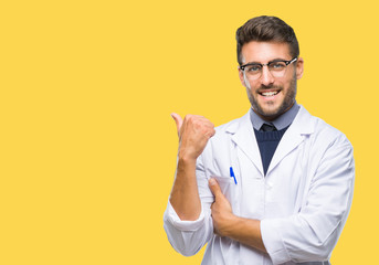 Young handsome man wearing doctor, scientis coat over isolated background smiling with happy face looking and pointing to the side with thumb up.