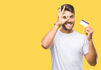 Young handsome man holding credit card over isolated background with happy face smiling doing ok...